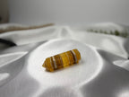 Treasured Energies yellow fluorite crystal tower with banded patterns resting on a white satin fabric background.