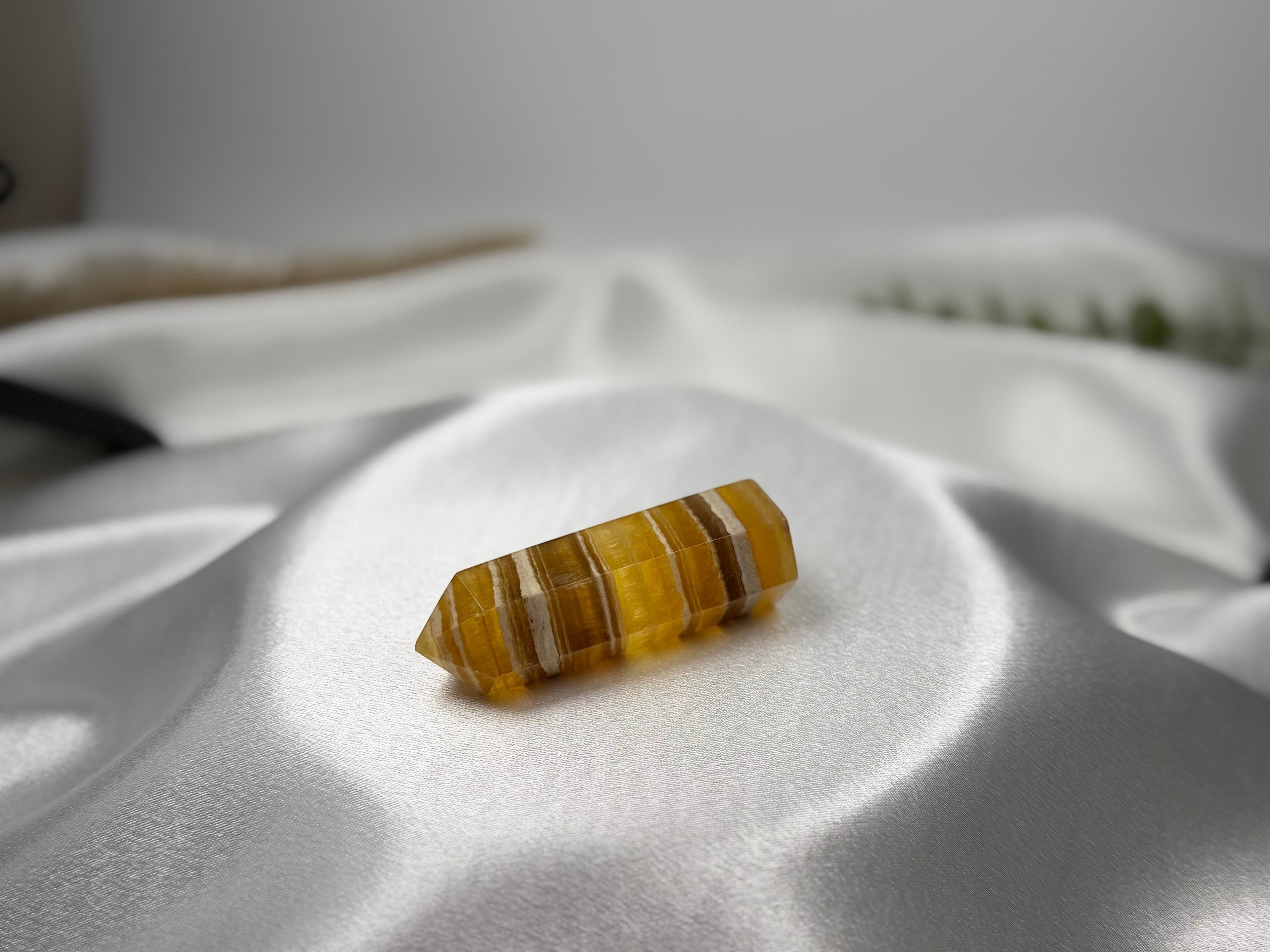 Treasured Energies yellow fluorite crystal tower with banded patterns resting on a white satin fabric background.