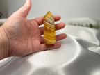 Treasured Energies yellow fluorite crystal tower held in a hand, showing banded golden patterns and a pointed tip.