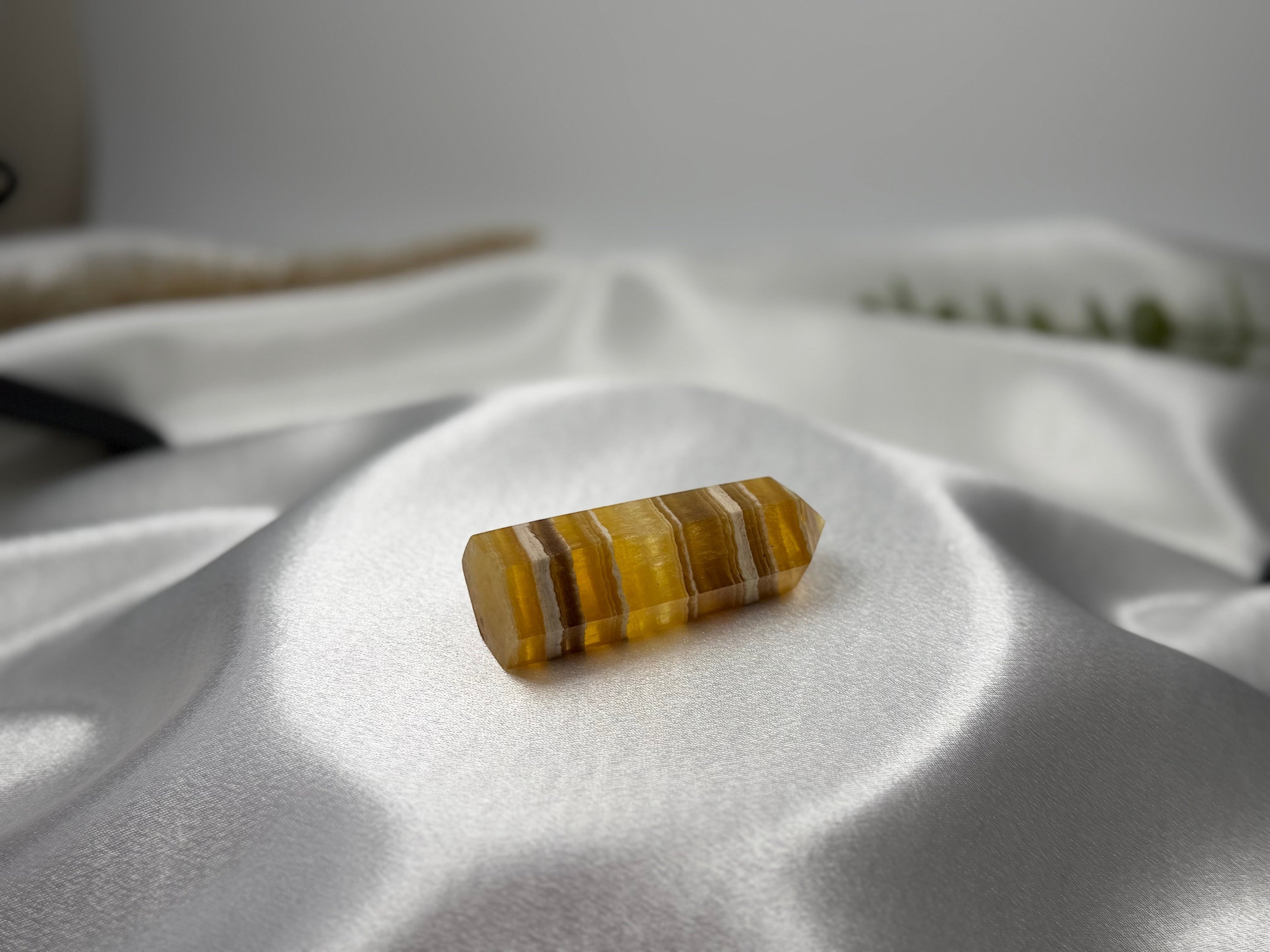 Treasured Energies yellow fluorite crystal tower with banded golden patterns resting on a smooth white satin fabric.