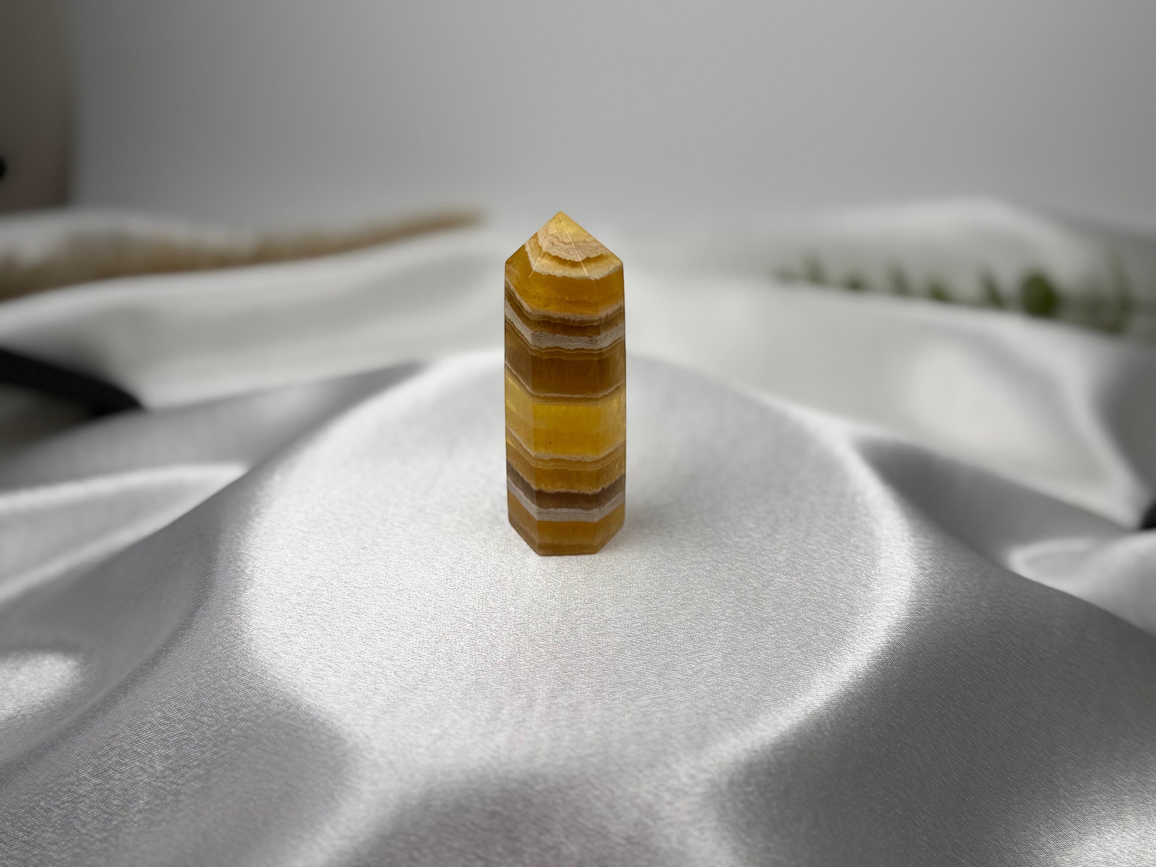 Treasured Energies yellow fluorite crystal tower with banded golden layers on a white satin background.
