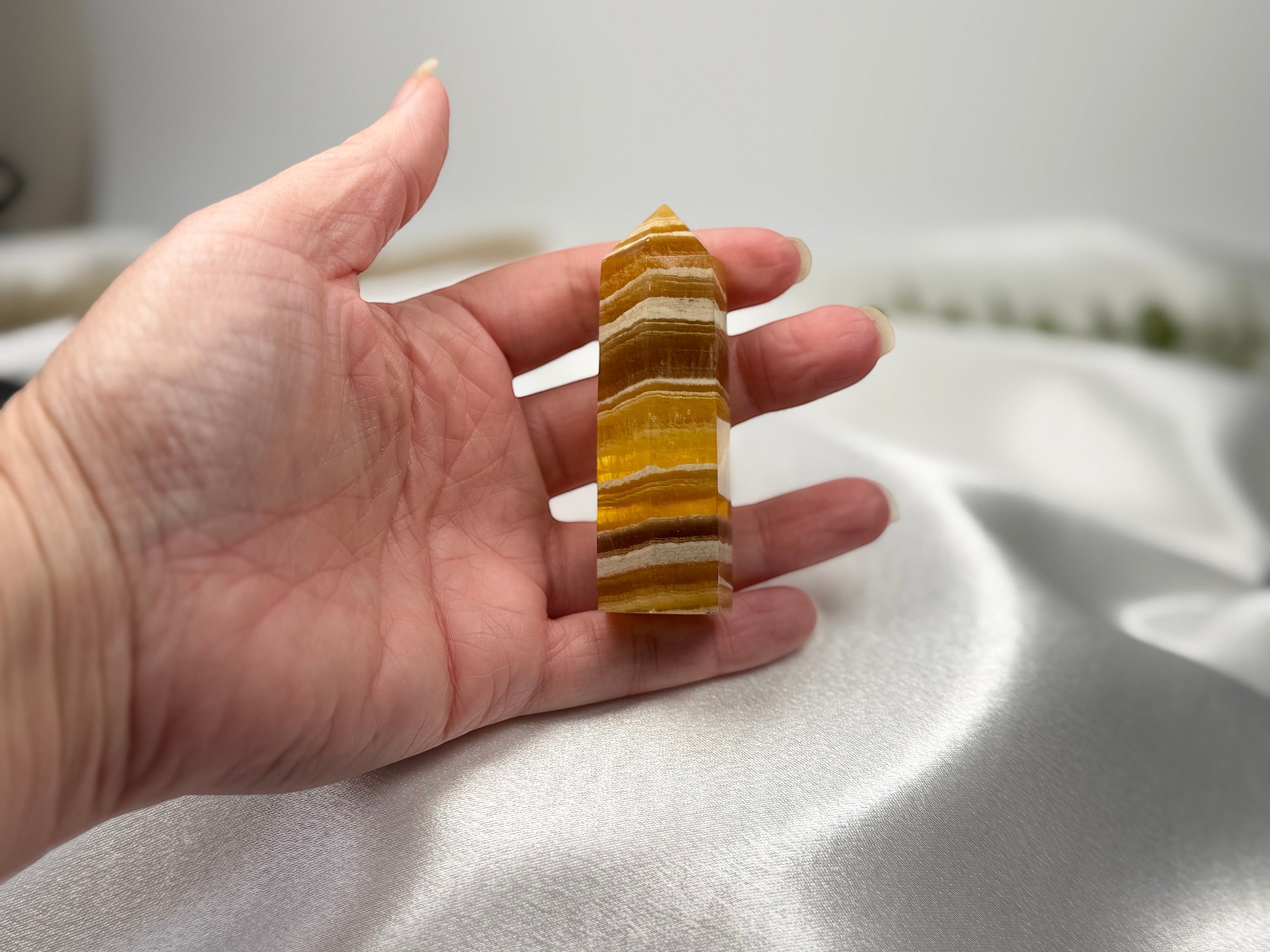 Treasured Energies yellow fluorite crystal tower held in a hand, showing banded golden and white natural stone layers.